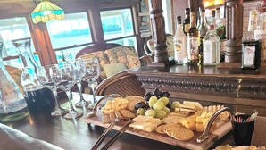 Zona de bar con una tabla de quesos y galletas, vasos y una variedad de botellas de licor.