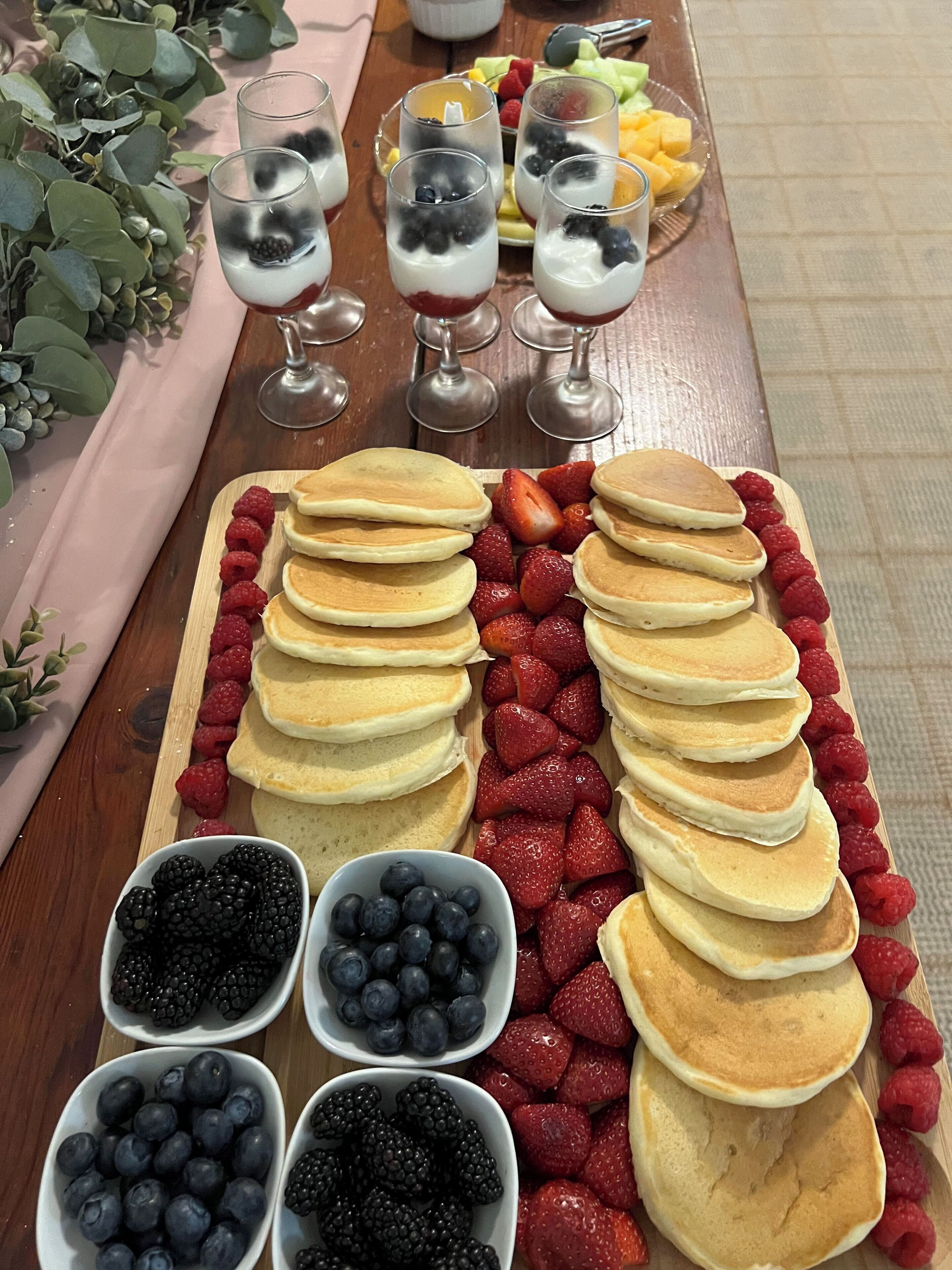 A breakfast spread with pancakes, berries, and fruit parfaits.