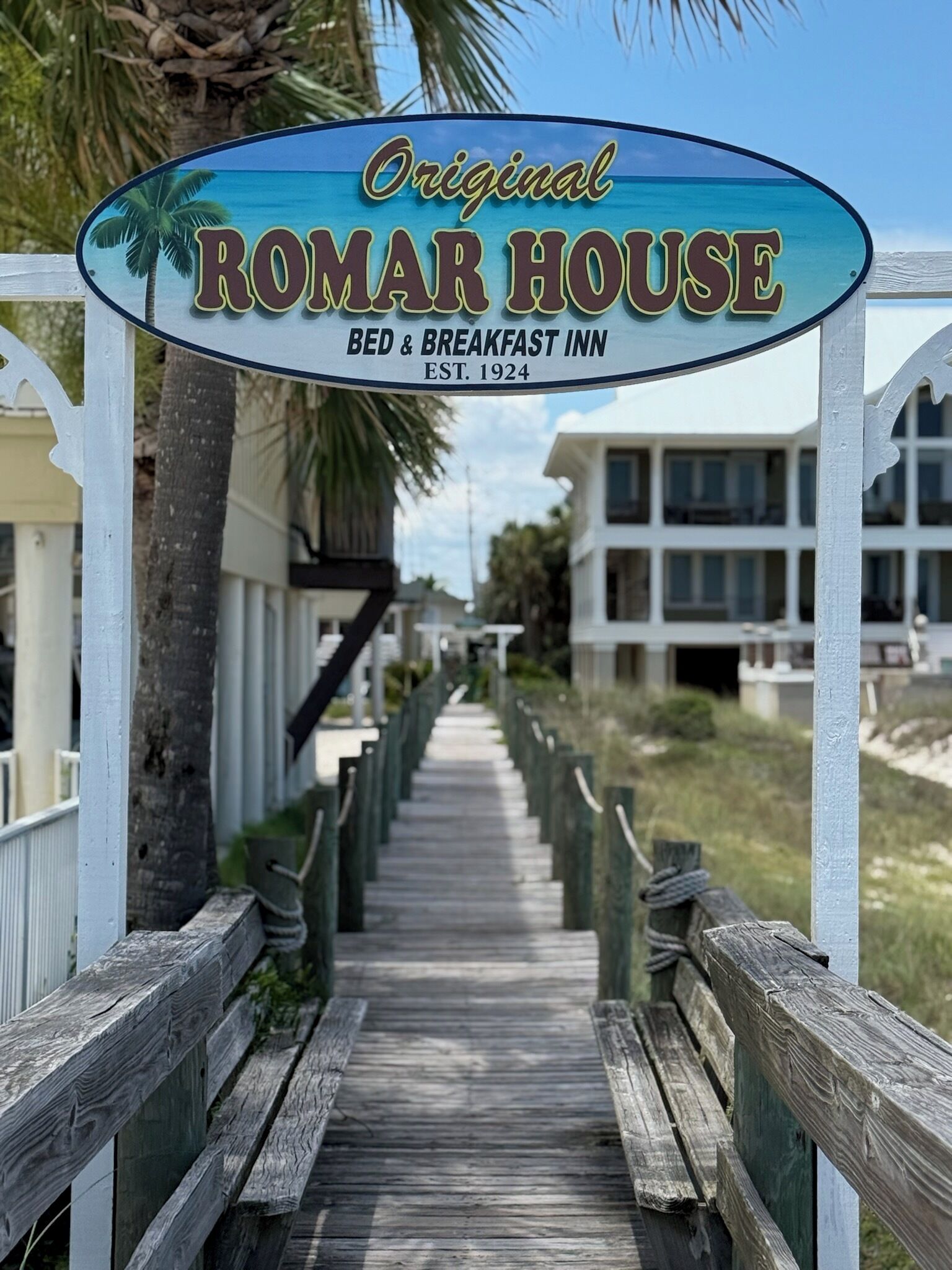 Een houten looppad dat leidt naar een gebouw met een bord waarop staat 'Original ROMAR HOUSE BED & BREAKFAST INN EST. 1924'.