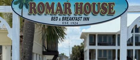 Een houten looppad dat leidt naar een gebouw met een bord waarop staat 'Original ROMAR HOUSE BED & BREAKFAST INN EST. 1924'.