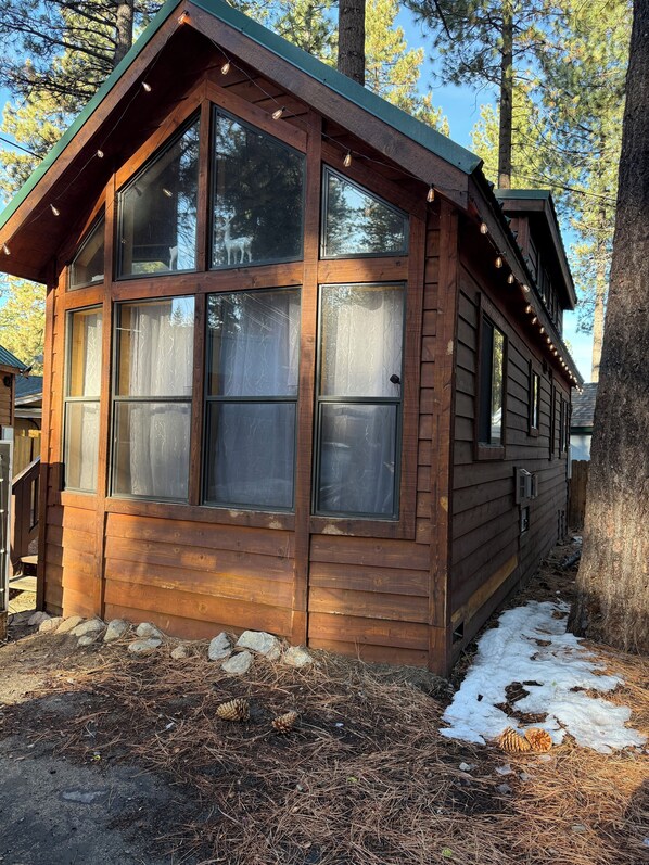 Una cabaña de madera con amplias ventanas, un porche y suelo cubierto de nieve.
