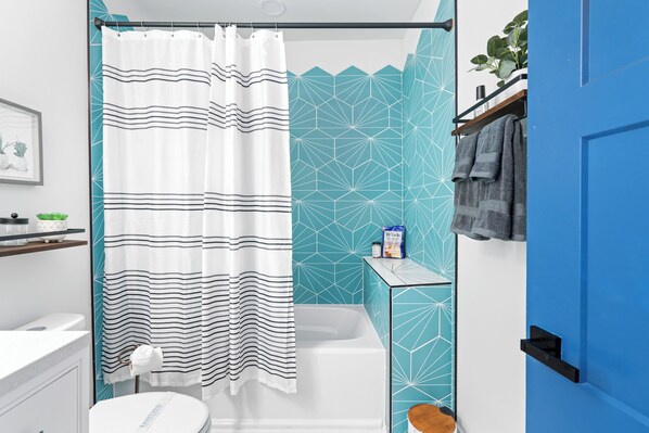 A bathroom with a white bathtub, a striped shower curtain, and a blue geometric wall design.