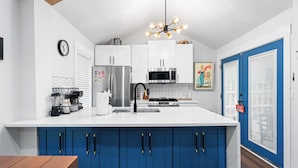 Uma cozinha moderna com armários brancos, uma ilha azul, eletrodomésticos de aço inoxidável e um lustre diferenciado.
