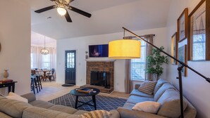 A living room with a sofa set, a fireplace, a ceiling fan, and a dining area in the background. - Charming Charlotte 3-bedroom house, Fenced Yard, 5 Mins to Carowinds, WiFi, Pets (Charlotte)