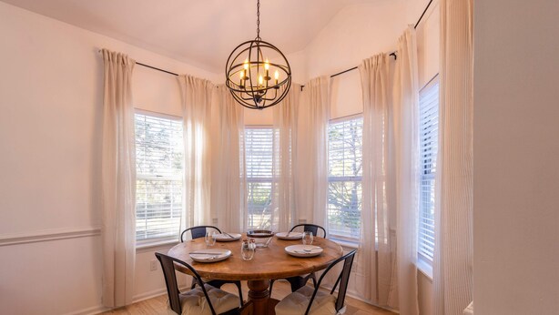 A dining room with a round wooden table, six chairs, and a chandelier. - Charming Charlotte 3-bedroom house, Fenced Yard, 5 Mins to Carowinds, WiFi, Pets (Charlotte)