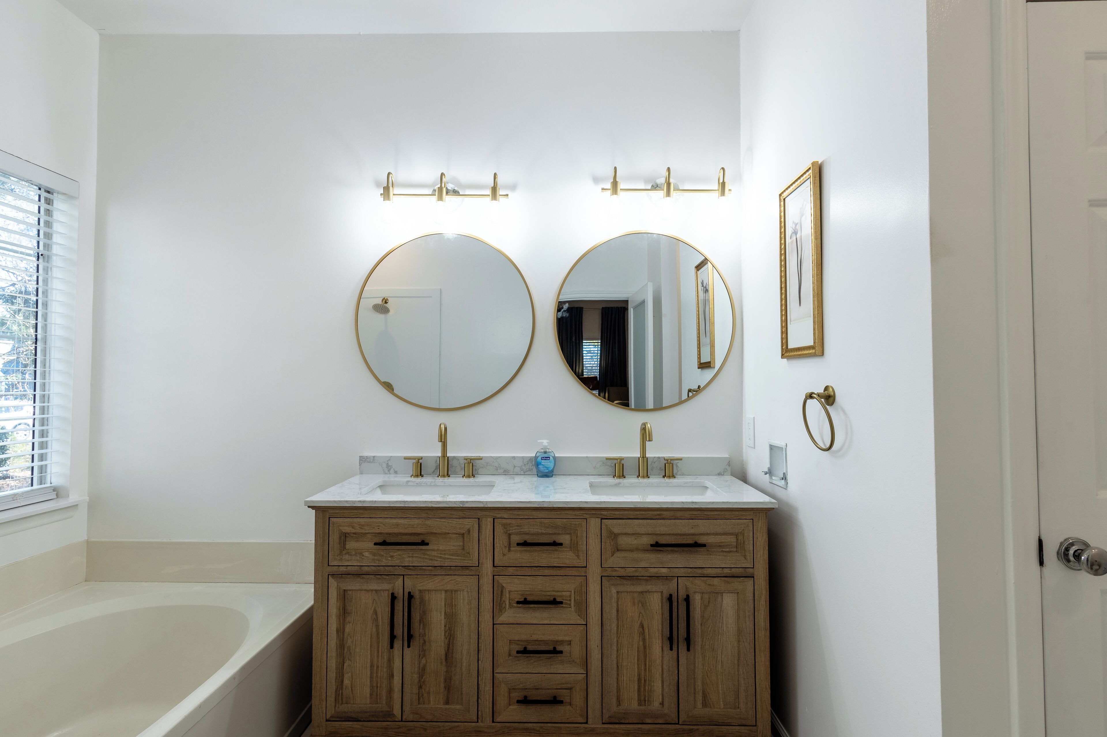 A bathroom with two sinks, wooden cabinets, a bathtub, and two wall-mounted mirrors.