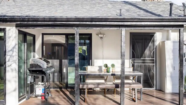 A modern outdoor patio with a grill, seating area, and a glass door leading to the interior.