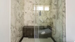 A glass-enclosed shower with marble walls and a tiled floor.