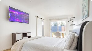 A modern bedroom with a bed, a TV mounted on the wall, a window with a view, and a chair by the window.