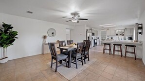 A spacious dining area with a high ceiling fan, a kitchen with white cabinets, and a bar area with stools.