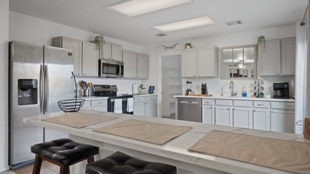 A modern kitchen with white cabinets, stainless steel appliances, a central island with stools, and overhead lighting.