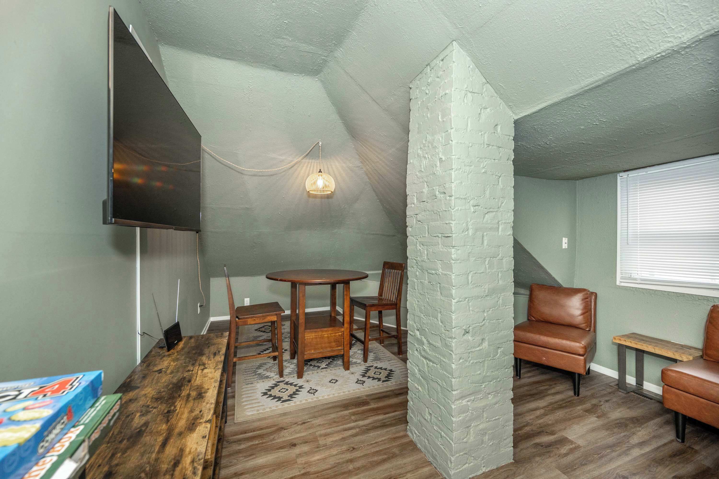 A cozy room with a wooden table and chairs, a white brick accent wall, and a television mounted on the wall.