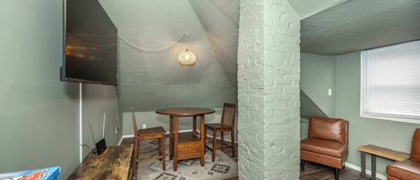 A cozy room with a wooden table and chairs, a white brick accent wall, and a television mounted on the wall.