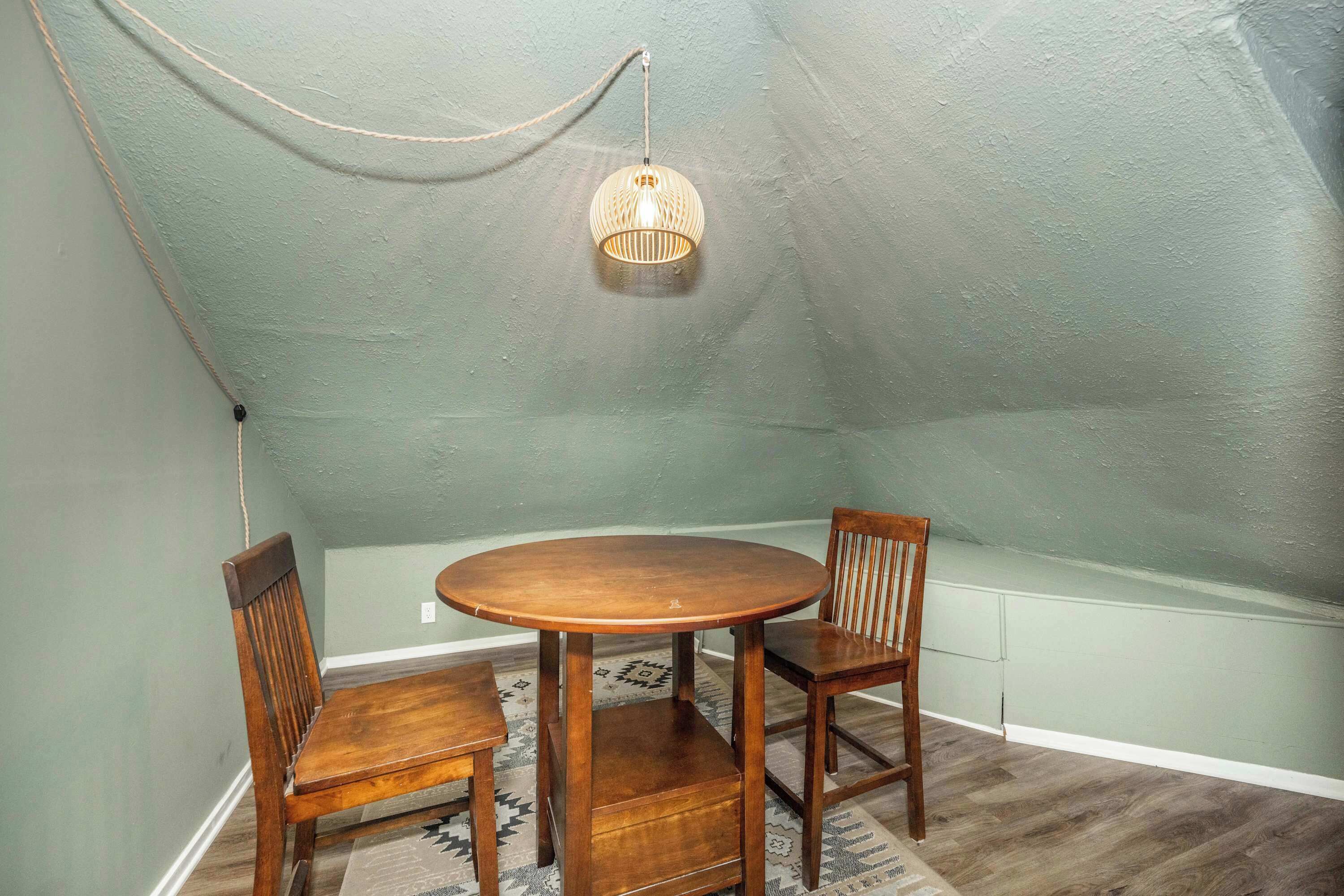 Et spiseområde med et rundt træbord, to stole, en hængende lampe og en bænk langs væggen.