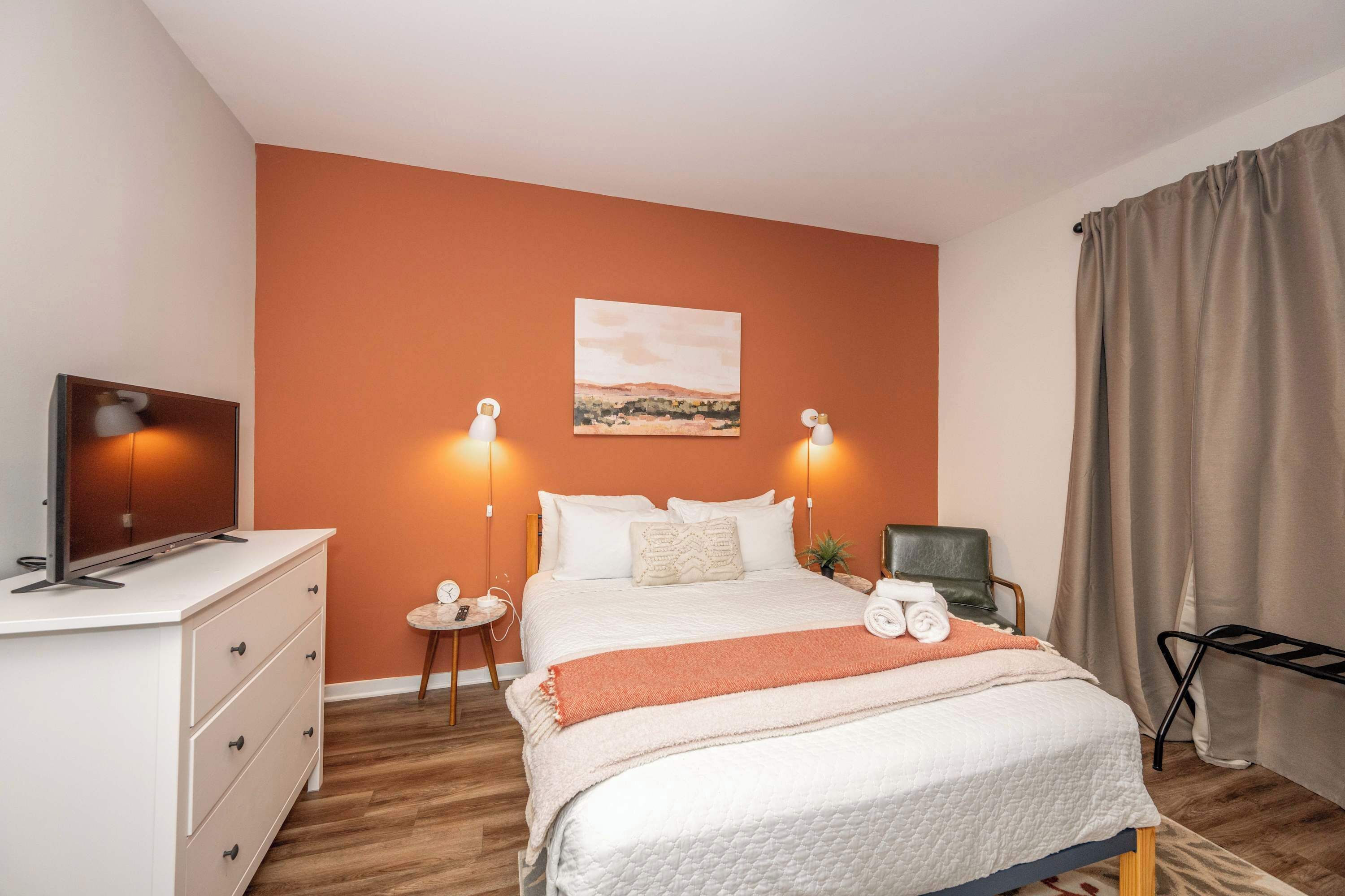 A hotel room with a large bed, a desk with a TV, and a painting on the wall.