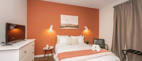 A hotel room with a large bed, a desk with a TV, and a painting on the wall.