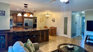 A modern kitchen with a central island, dining area with chairs, a sofa, and a TV in a living room.
