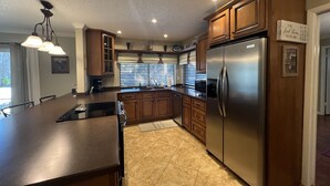 A modern kitchen with a central island, stainless steel appliances, wooden cabinets, and a large window with blinds.