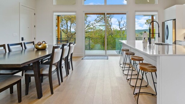 A spacious kitchen with a dining area, large windows, and a high ceiling fan.
