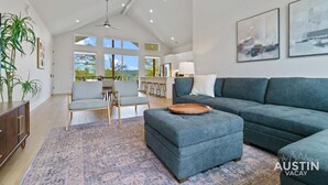 A spacious living room with a large grey sofa, a wooden coffee table, and a dining area with chairs.
