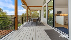 A spacious balcony with a table and chairs, a kitchen area with a microwave, and a view of the surrounding landscape.