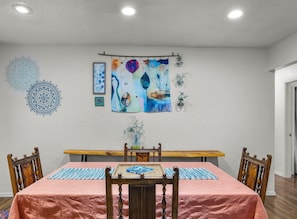 A dining area with a table set for four, a bench, and wall art including a mandala and abstract paintings.