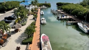 A marina with boats docked, a pathway leading to a building with a blue roof, and a clear view of the sea.