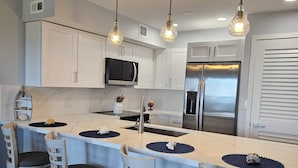 A modern kitchen with white cabinets, a stainless steel refrigerator, and a central island with bar stools.