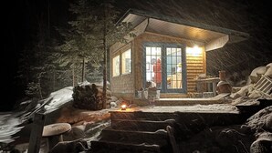 Una baita con facciata in legno, un portico e interni illuminati visibili dalle finestre.