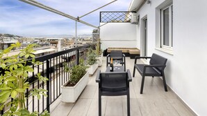 Een balkon met uitzicht op de stad, met een tafel, stoelen, plantenbakken en een hekwerk.