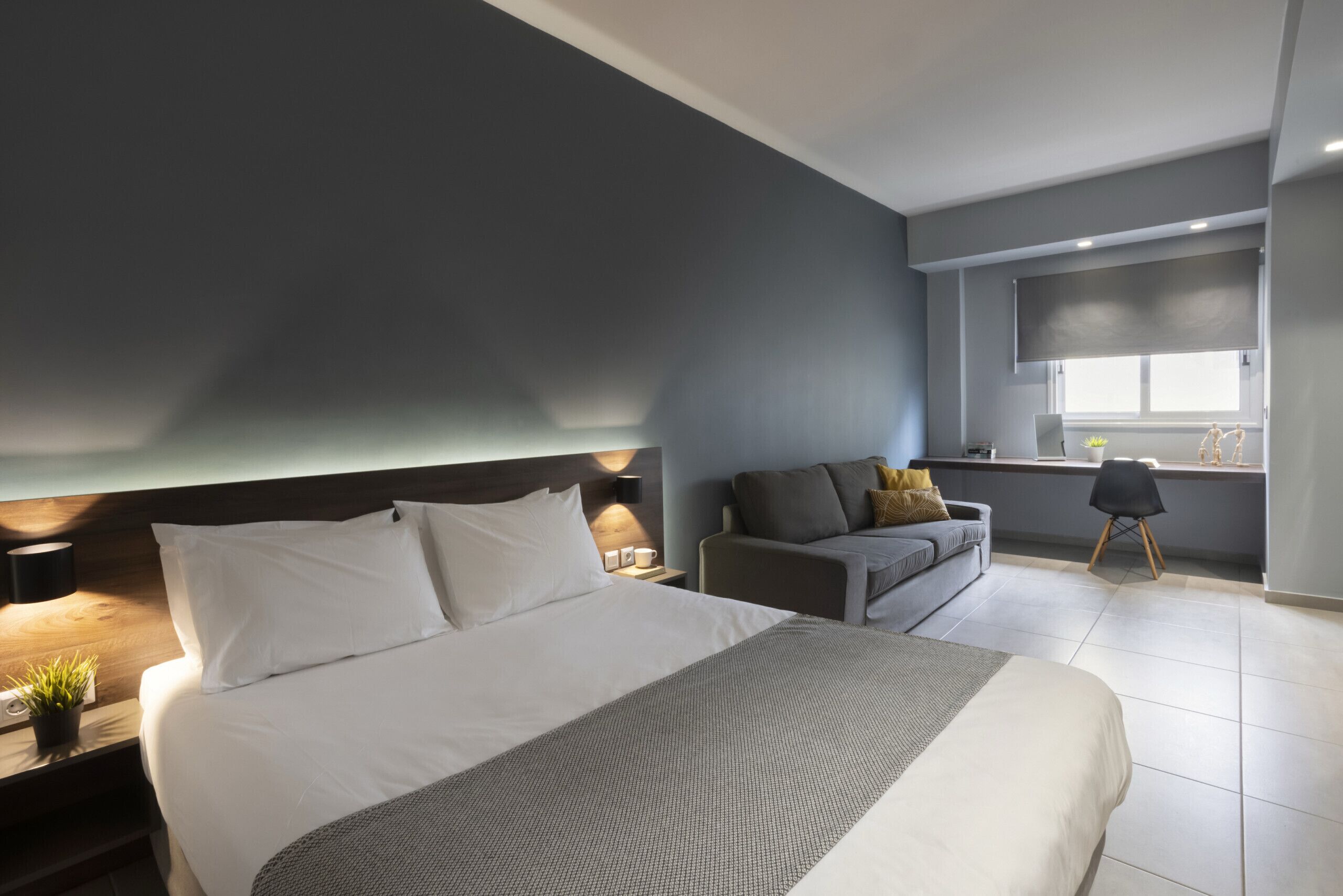 Une chambre moderne avec un grand lit, un canapé, une petite table et une fenêtre avec des stores.