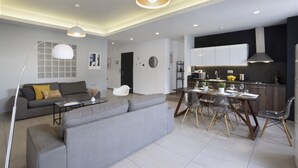 Een moderne woonkamer met een grijze bank, een eettafel met stoelen, en een keuken met kasten en apparatuur.