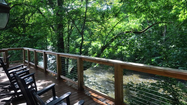 Una terraza de madera con bancos que da a un río, rodeada de abundante vegetación.