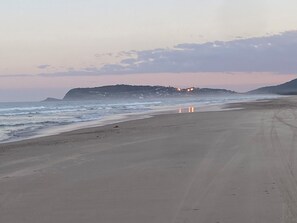 A beach with a long stretch of sand, waves, and a distant hill with lights. - Coastal Escape (South Kempsey)