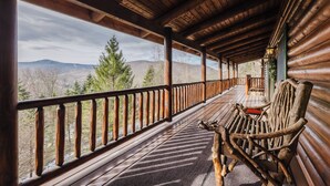 A wooden deck with a view of mountains, a wooden bench, and a railing.