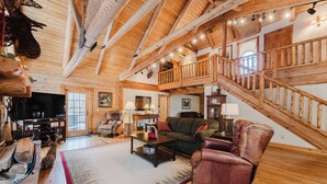 A spacious living room with a wooden staircase, a television, and comfortable seating.