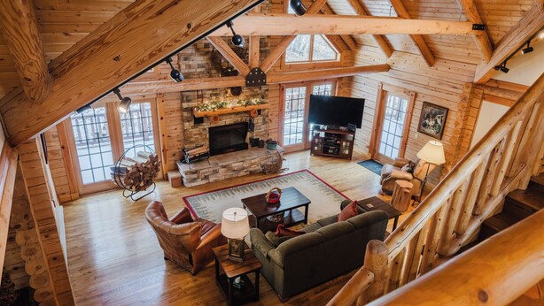 A spacious living room with a fireplace, wooden beams, a television, and a staircase.