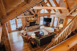 A spacious living room with a fireplace, wooden beams, a television, and a staircase. - Luxury 3 Bedroom Log Cabin in Snowshoe Resort’s Hawthorne Valley - Sleeps 8 - 10 (Snowshoe)