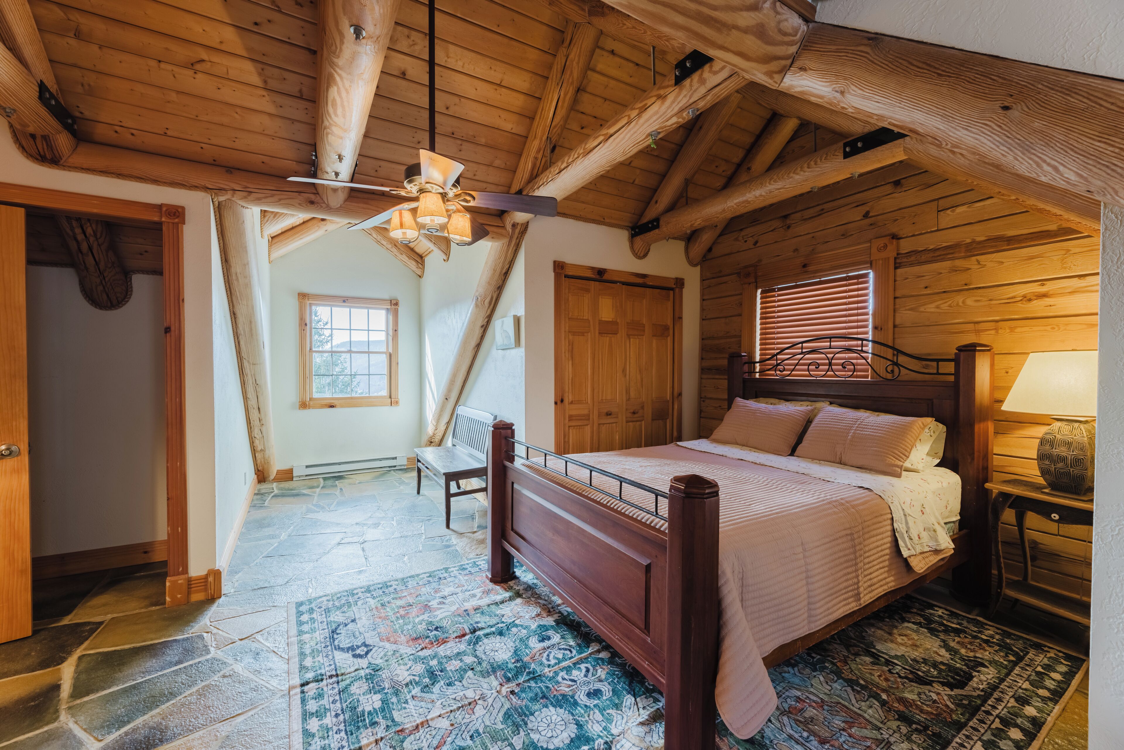Une chambre dans une cabane en bois, avec un lit, un banc et un ventilateur de plafond.