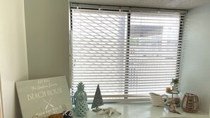 Ein Fenster mit horizontalen Jalousien, ein Schild am Fensterbrett und Dekorationen wie eine Ananas, ein Seestern und eine kleine Pflanze.
