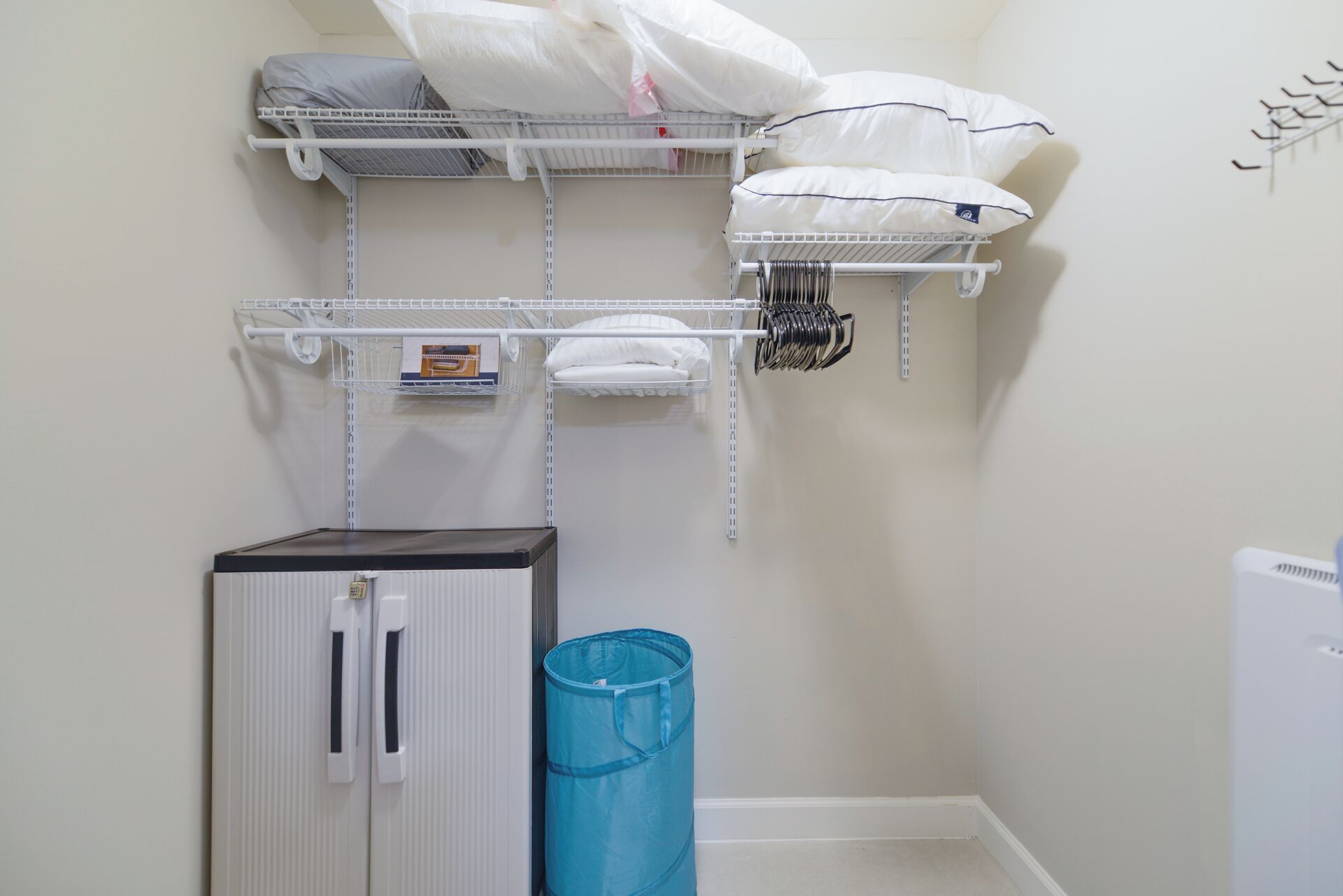 A laundry room with shelves holding laundry supplies, a blue trash bin, and a white cabinet.