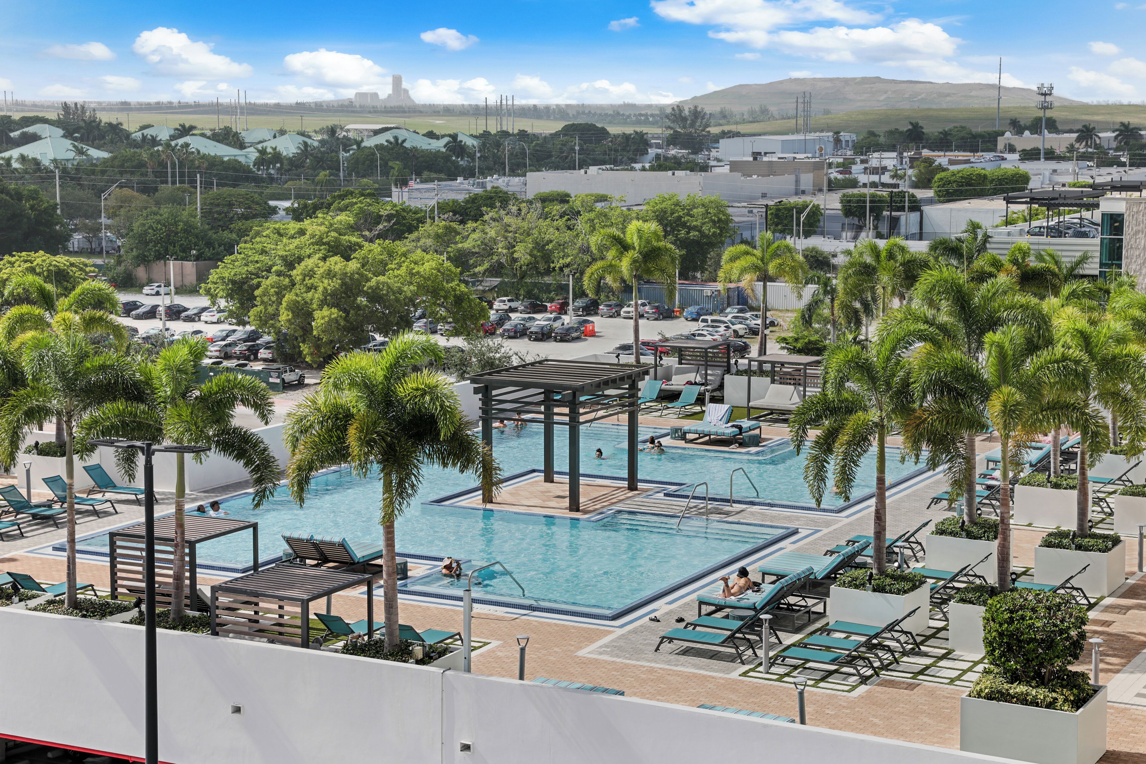 A rooftop pool area with multiple swimming pools, lounge chairs, and palm trees.