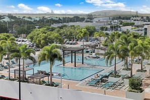 Un área de piscina en la azotea con múltiples piscinas, sillas de descanso y palmeras.