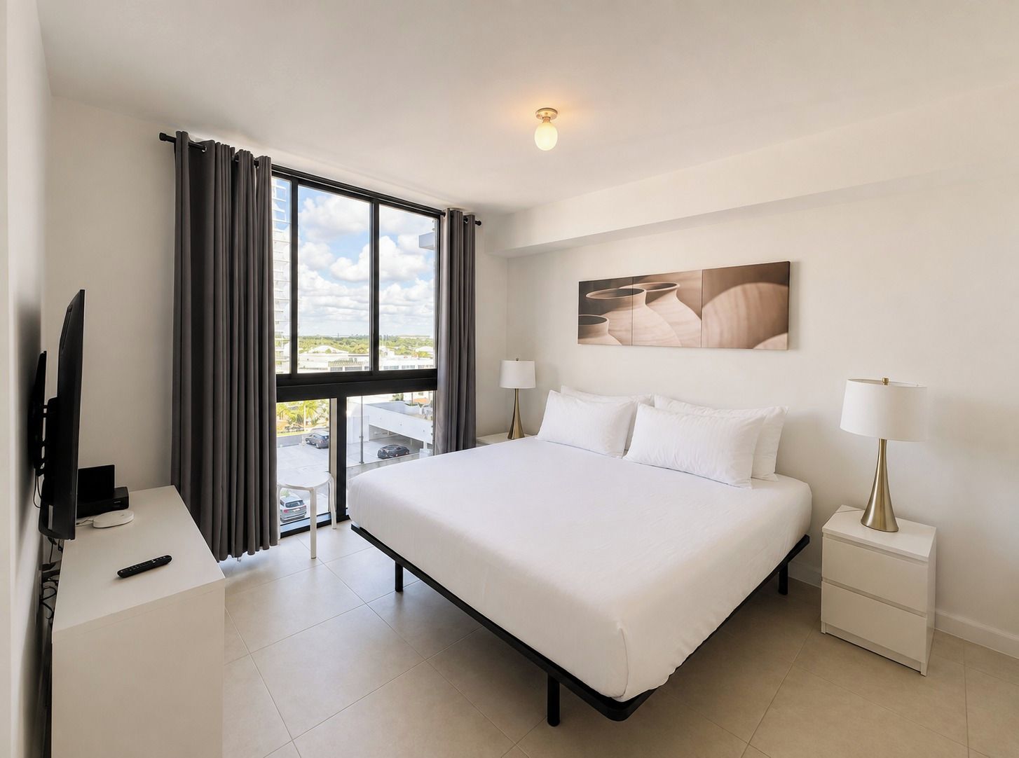 Una habitación de hotel con una cama, un escritorio con televisor, una lámpara y un cuadro en la pared.