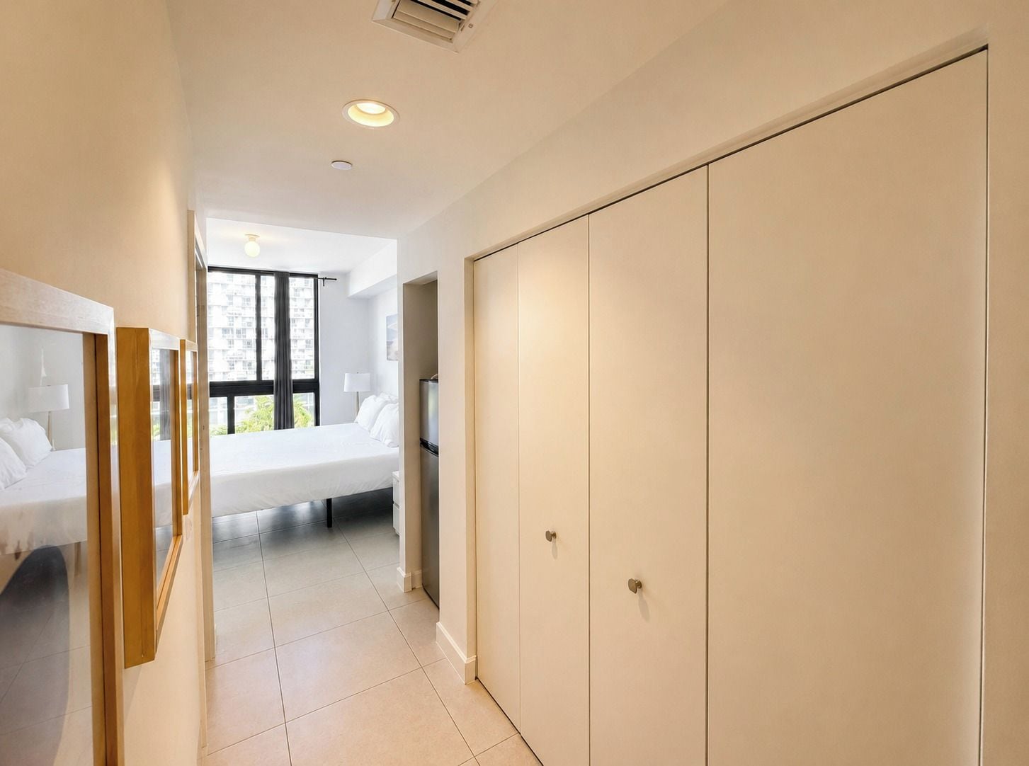 Une chambre d’hôtel avec un lit, une armoire et une fenêtre donnant sur des immeubles.