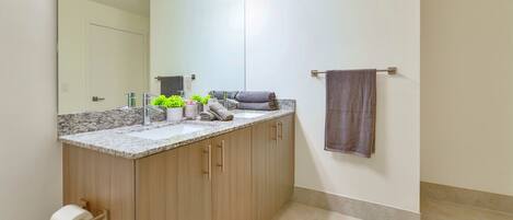 A bathroom with a marble countertop, a sink, a mirror, and a towel rack.