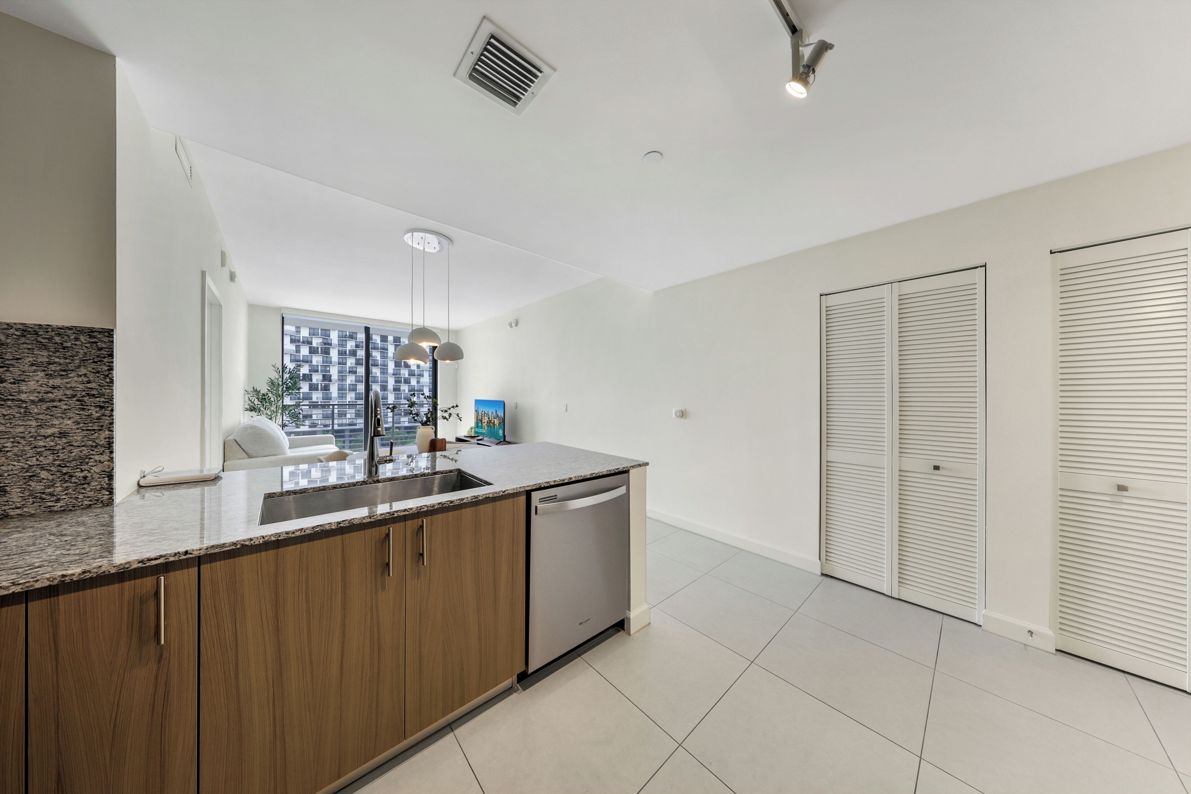 A modern kitchen with a granite countertop, wooden cabinets, a dishwasher, and a window with a city view.
