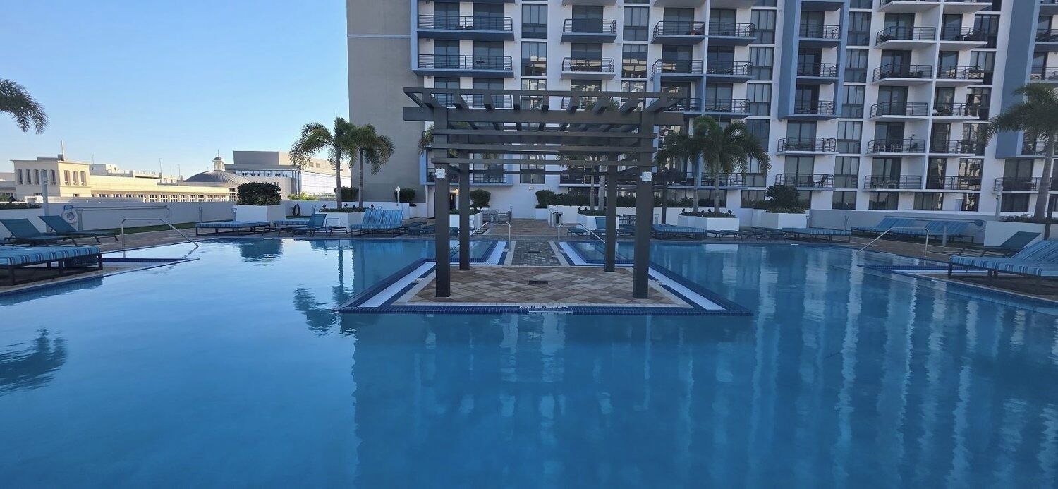 A hotel pool area with a pergola, lounge chairs, and a multi-story building in the background.