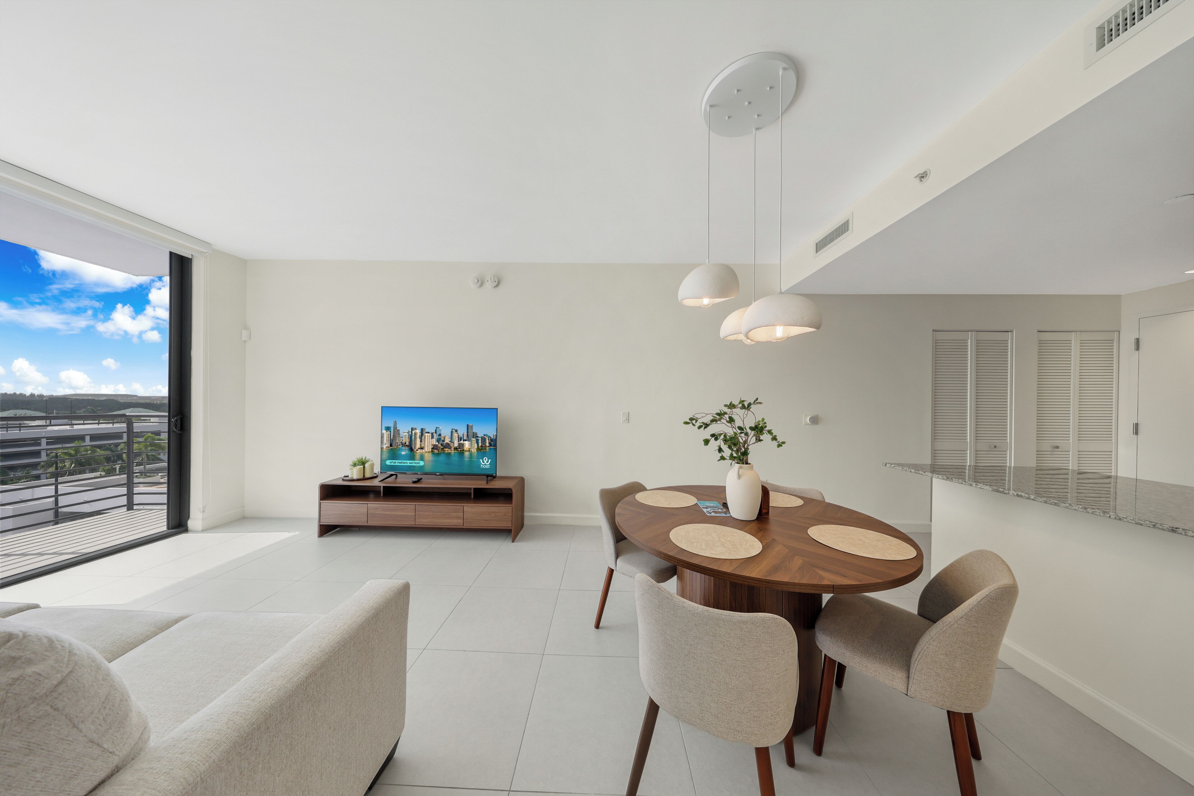 A modern living room with a dining area, a flat-screen TV, and a balcony with a city view.