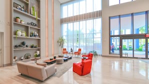 A spacious lobby with a beige sofa, red chairs, and a large bookshelf filled with decorative items. - 5350 Nw Downtown - Doral Building - We Host (Miami)